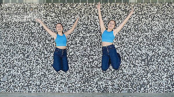 Glückliche Schwestern springen vor einer strukturierten Wand