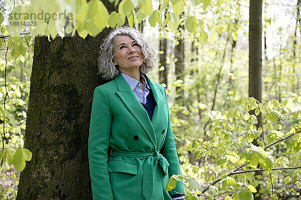 Nachdenkliche Frau träumt im Wald und trägt einen grünen Mantel