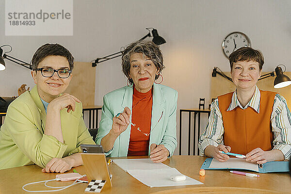 Drei Geschäftsfrauen sitzen am Tisch und schauen in die Kamera