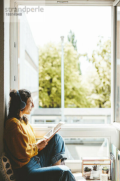 Frau mit Tablet-PC sitzt zu Hause am Fenster