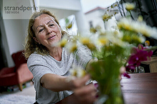 Lächelnde ältere Frau  die zu Hause Blumen berührt