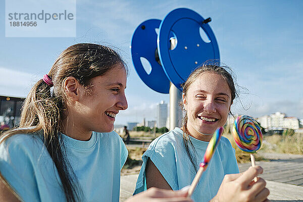 Cheerful twin sisters enjoying lollipop candy at beach