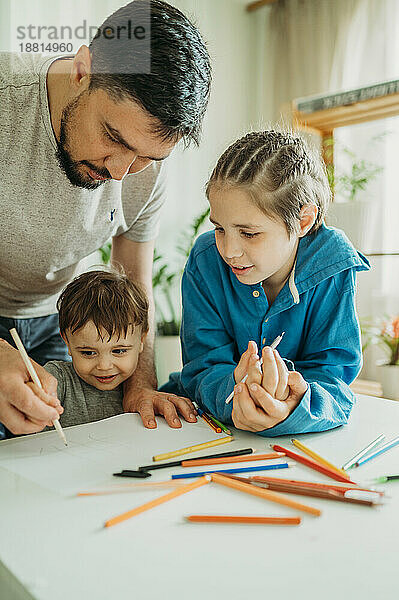 Junge lehnt sich an seinen Bruder und lernt zu Hause mit seinem Vater das Zeichnen
