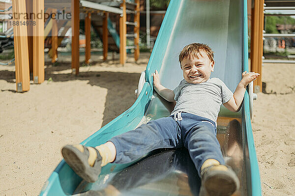 Carefree boy playing on slide in playground at sunny day