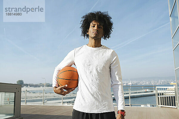 Selbstbewusster junger Athlet  der an einem sonnigen Tag Basketball spielt
