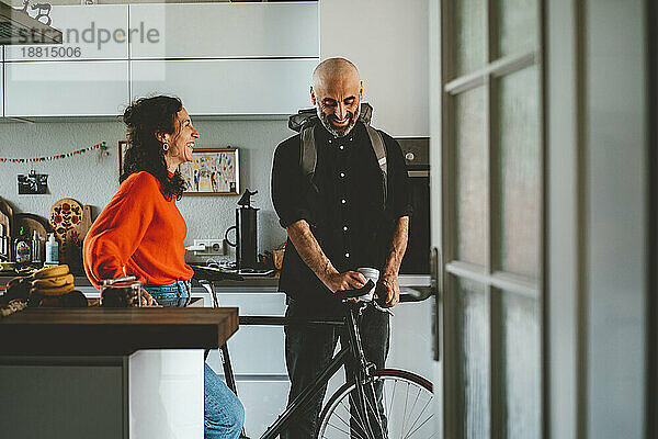 Lächelnde Frau spricht mit Mann  der zu Hause mit dem Fahrrad steht