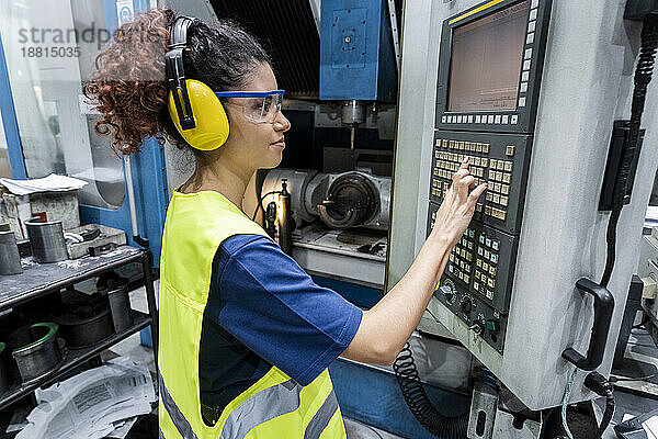 Ingenieur in Arbeitsschutzkleidung bedient CNC-Maschine in moderner Fabrik