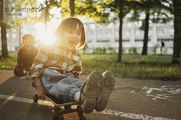 Fröhlicher Junge  der auf der Straße Skateboard fährt