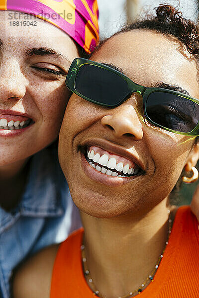 Fröhliche Frau mit Sonnenbrille von einer Freundin an einem sonnigen Tag