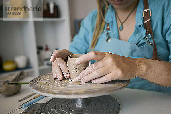 Kunsthandwerkerin formt Tonbecher auf Töpferscheibe in Werkstatt