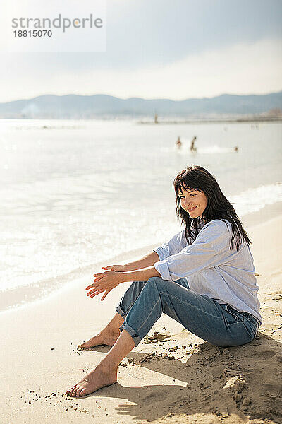 Lächelnde Frau  die an einem sonnigen Tag auf Sand sitzt