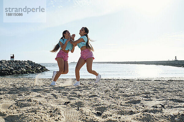 Sorglose Zwillingsschwestern in kurzen Hosen spielen am Strand