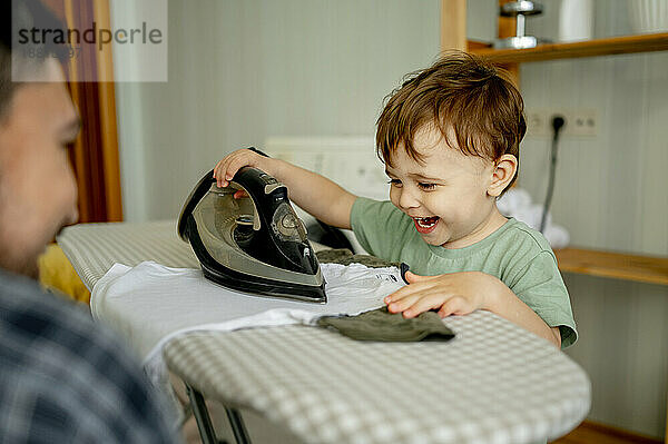 Happy cute boy ironing clothes with father at home