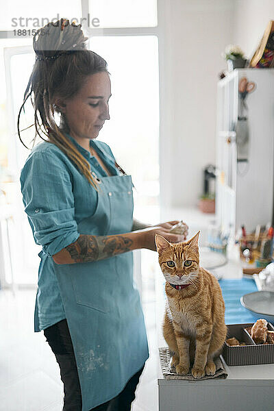Junge Frau modelliert mit Ton  während eine Katze an der Werkbank sitzt
