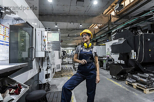 Lächelnder Wartungsingenieur steht neben der CNC-Maschine in einer modernen Fabrik