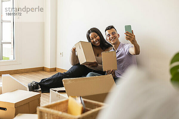 Glückliches Paar macht Selfie mit Pappkartons im neuen Zuhause