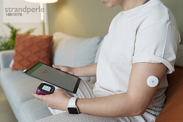 Frau mit Blutzuckermessgerät und Tablet-PC sitzt zu Hause
