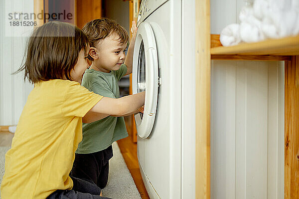 Glücklicher Junge mit Bruder  der zu Hause die Waschmaschine benutzt