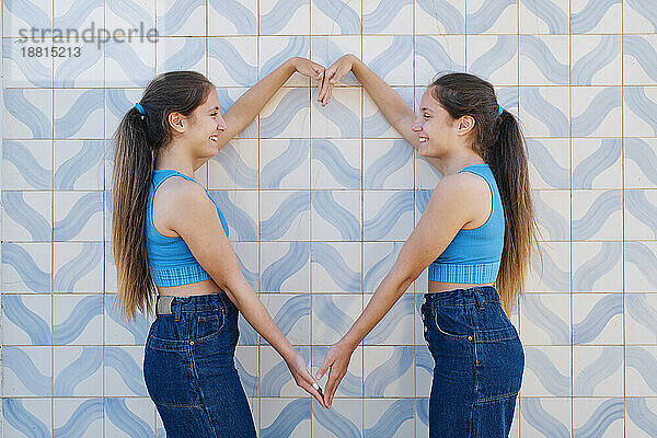 Glückliche Schwestern gestikulieren herzförmig vor der Wand