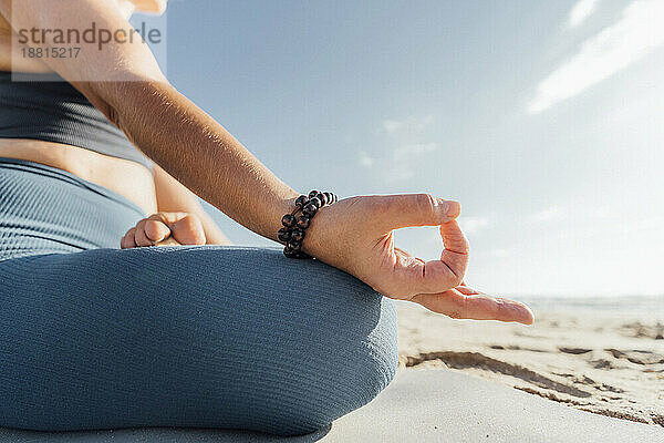 Frau mit Armband übt Lotussitz am Strand