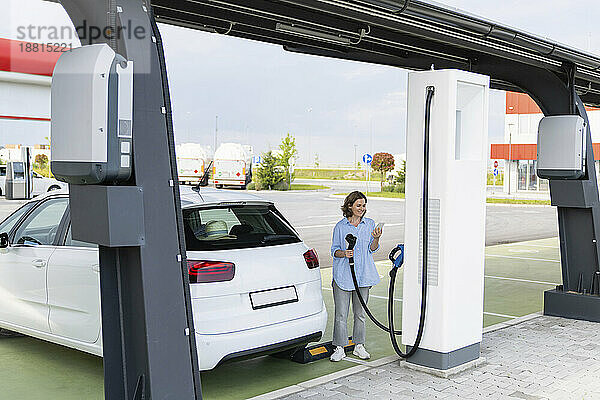 Woman standing near electric car at station
