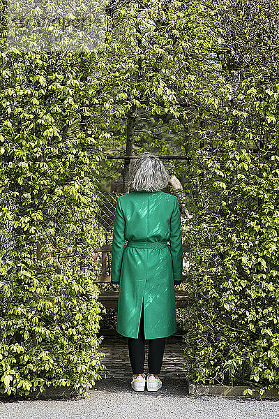 Ältere Frau steht in Plat Arcade und trägt grünen Mantel  Rückansicht