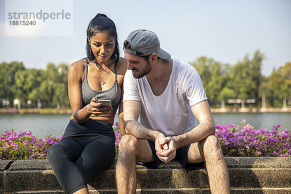 Man looking at smart phone held by woman sitting on bench