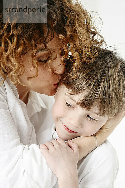 Mutter mit lockigem Haar küsst Sohn
