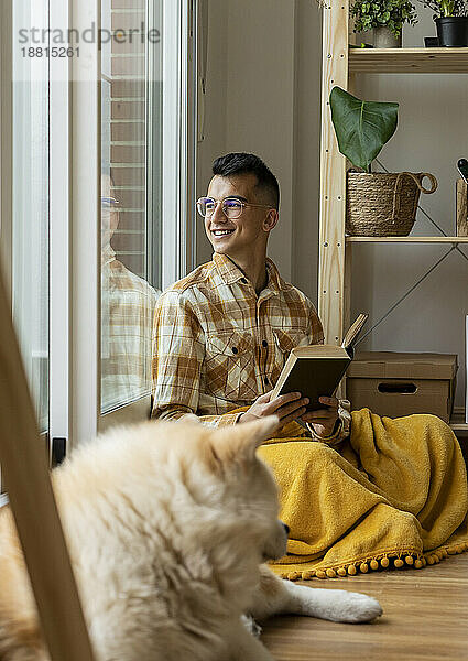 Smiling man with book looking out of window at home