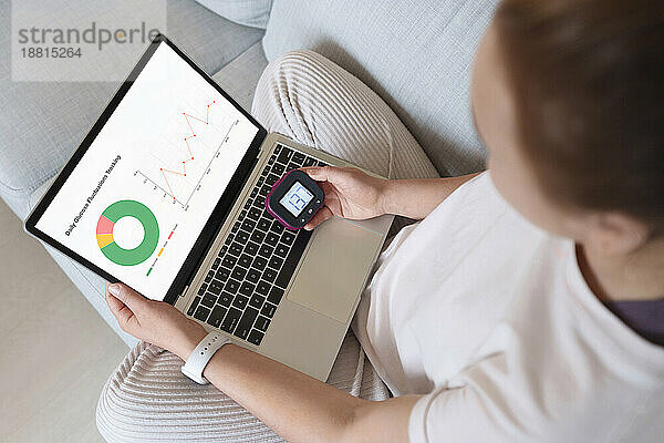 Woman with diabetes sitting on couch with laptop and glucometer at home