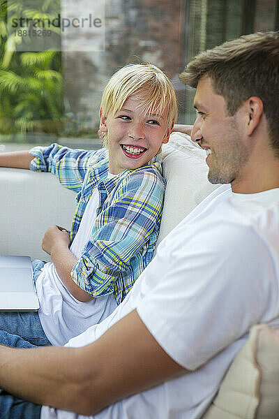 Happy boy with father sitting on sofa at home
