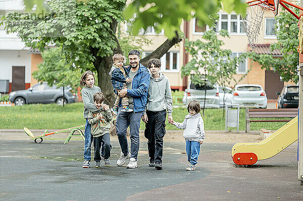 Glücklicher Vater geht mit Kindern auf dem Spielplatz spazieren
