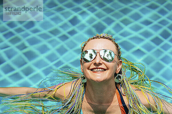 Glückliche Frau mit Sonnenbrille entspannt im Schwimmbad
