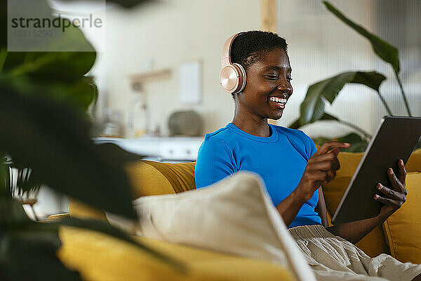 Glücklicher junger Freiberufler mit Tablet-PC auf dem Sofa