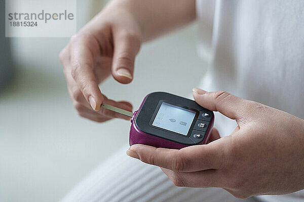 Hände einer Frau  die zu Hause ein digitales Glukometer verwendet