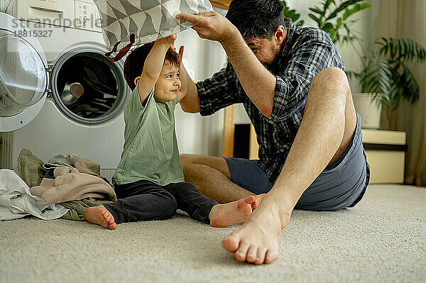 Glücklicher Vater und Sohn  die Spaß mit Wäschekorb haben und zu Hause Wäsche in der Maschine waschen