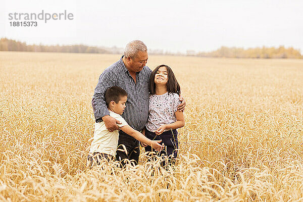 Bauer umarmt Enkelkinder  die inmitten von Feldfrüchten auf Weizenfarm stehen