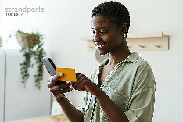 Glückliche Frau  die zu Hause per Kreditkarte auf dem Mobiltelefon bezahlt