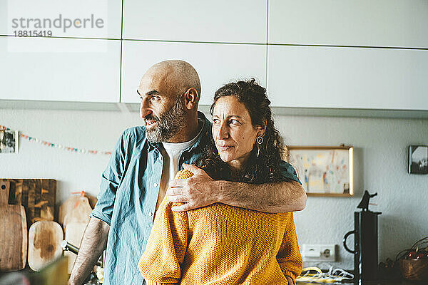 Nachdenklicher Mann mit Arm um Frau in der heimischen Küche