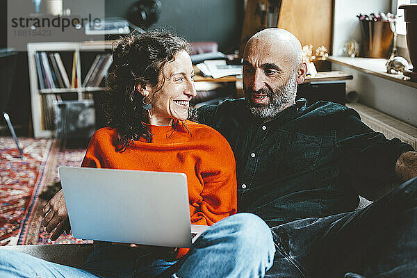Happy woman sharing laptop with man sitting at home