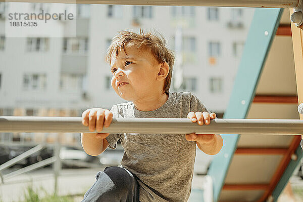 Neugieriger Junge hält Stange und klettert auf Spielplatz