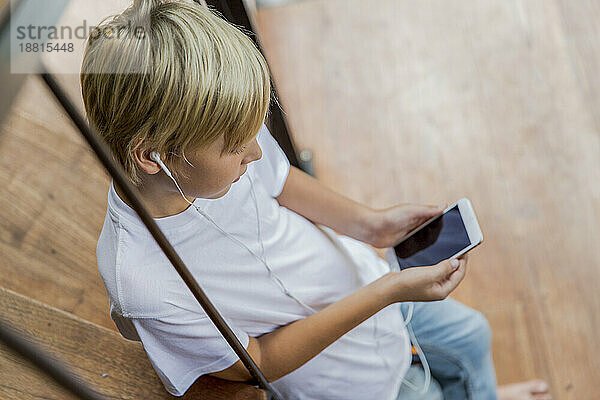 Junge trägt In-Ear-Kopfhörer und benutzt zu Hause sein Smartphone