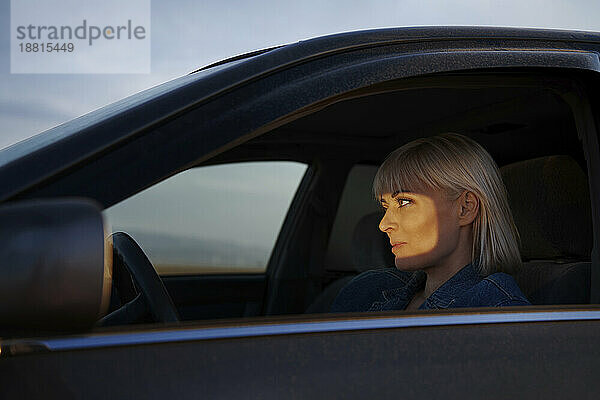 Blond woman driving car seen through window