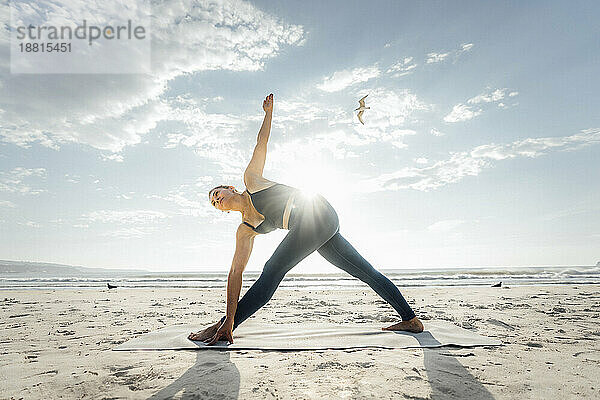 Frau übt Trikonasana-Pose am Strand an einem sonnigen Tag
