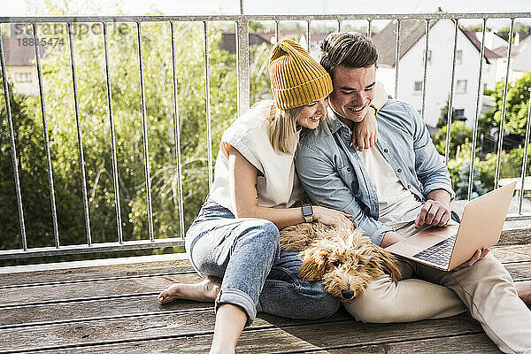 Glückliches junges Paar benutzt gemeinsam Laptop auf dem Balkon