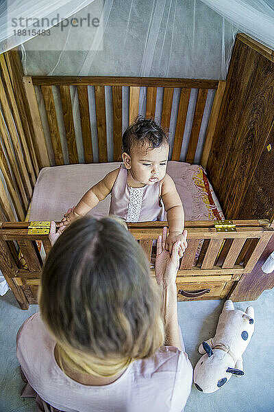 Mother with baby daughter playing in crib at home