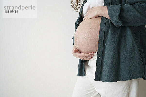 Schwangere Frau berührt Bauch vor Wand