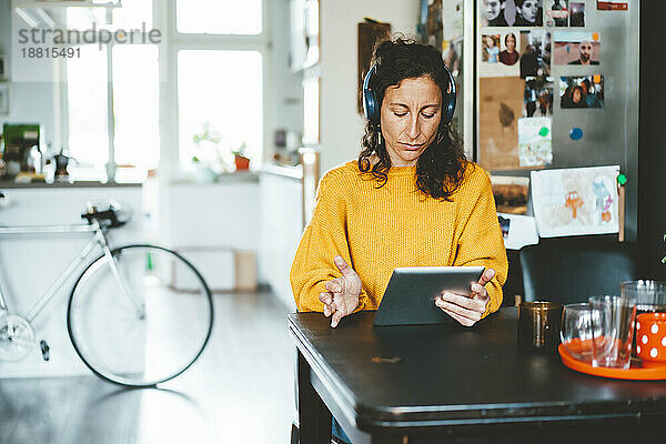 Frau mit kabellosen Kopfhörern und Tablet-PC sitzt zu Hause