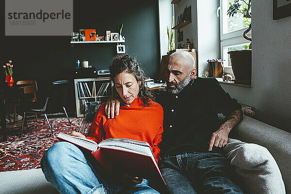 Frau teilt Buch mit Mann  der zu Hause auf dem Sofa sitzt