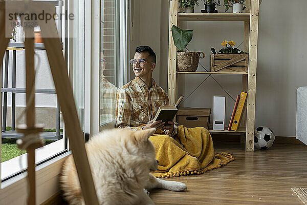 Smiling man holding book looking out of window at home